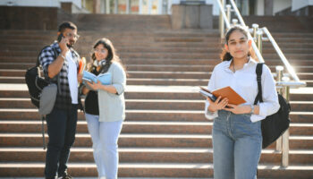 Three international students standing and holding a books.